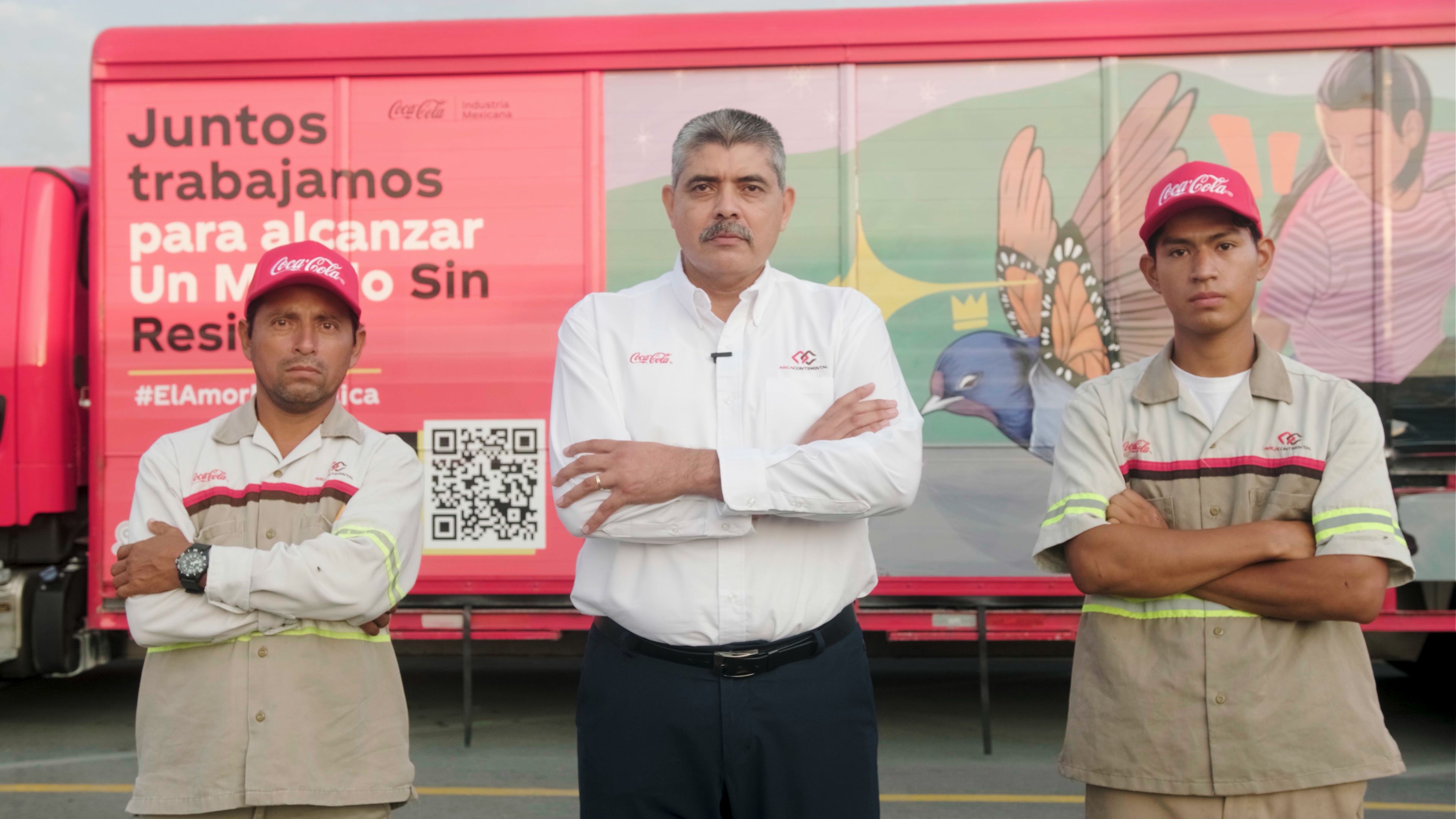 Tres hombres posan con los brazos cruzados delante de un camión de Coca-Cola