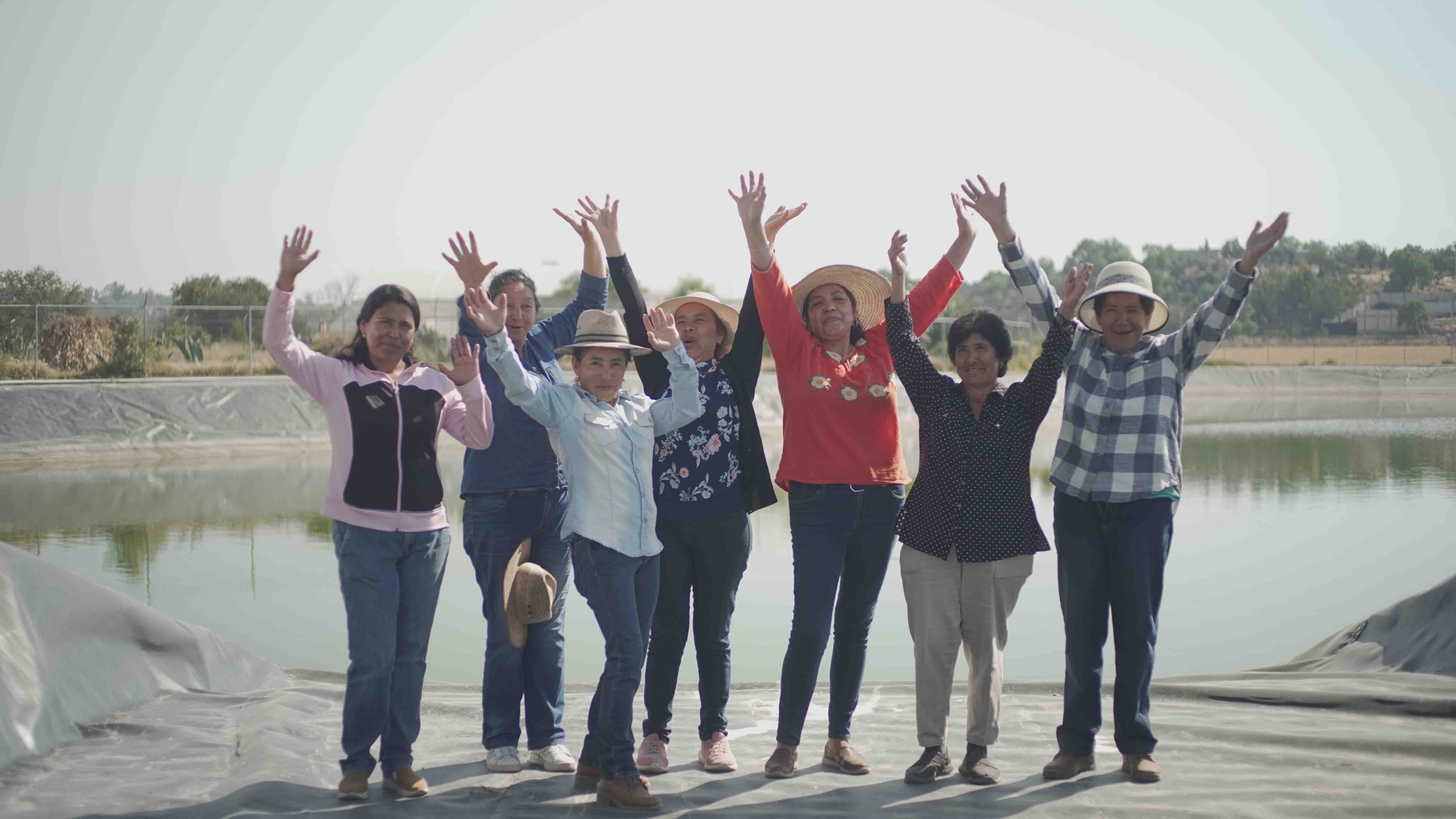 Mujeres saludan a cámara, en la base de una olla captadora