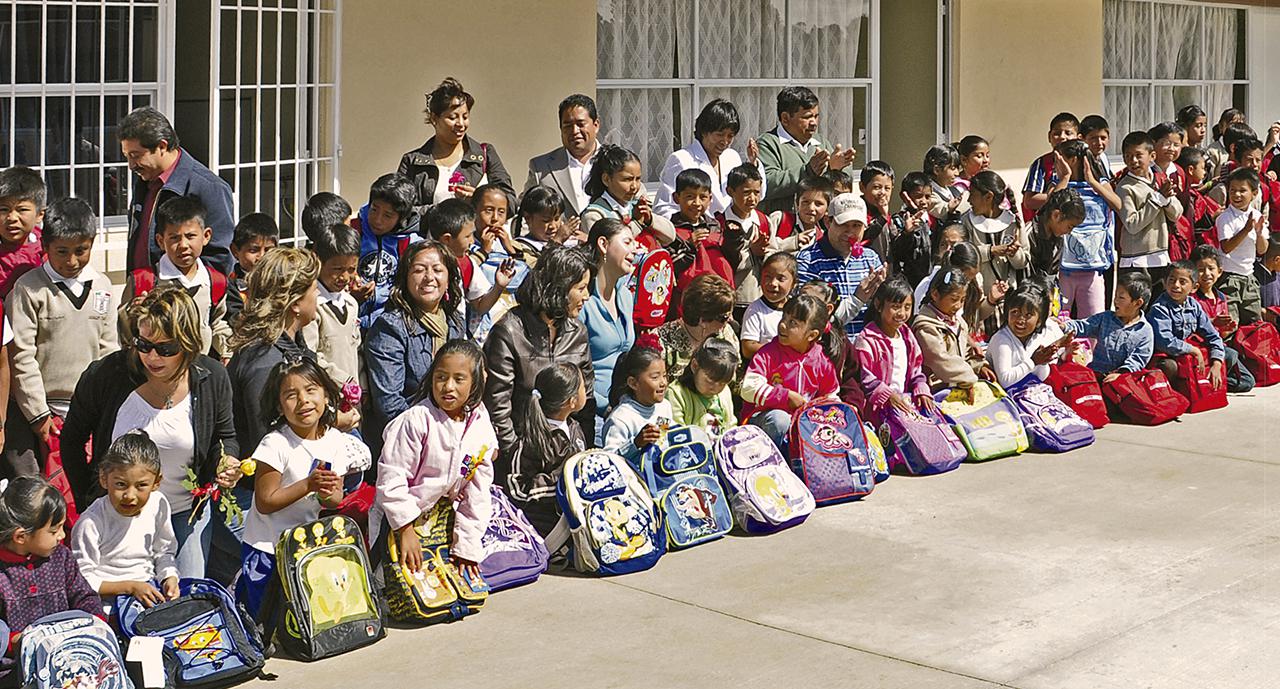 Niños sentados frente a su escuela, aplauden con alegría