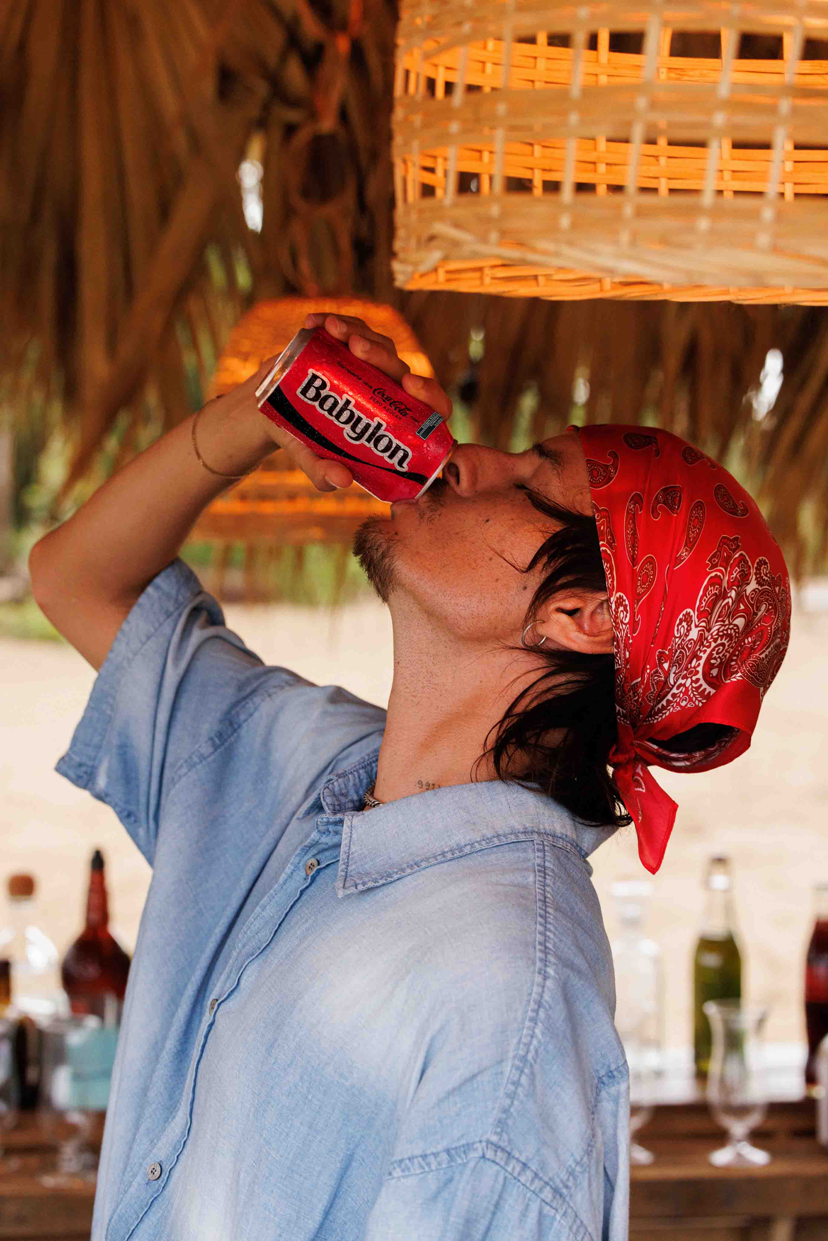 Danny Ocean con bandana roja y camisa bebiendo de una lata de Coca-Cola, que tiene escrita la palabra "Babylon".