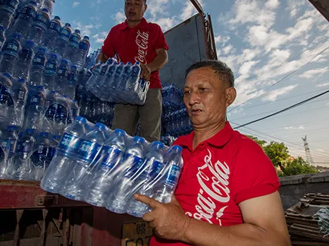 Dua orang lelaki sedang memunggah botol air yang dibungkus dari trak