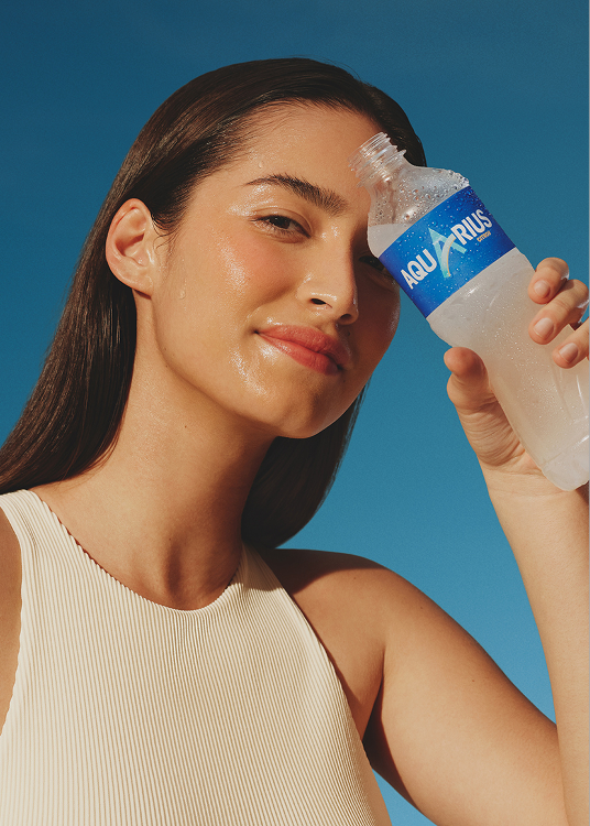 Een persoon drinkt water uit een fles tegen een blauwe achtergrond, met het gezicht onscherp gemaakt.