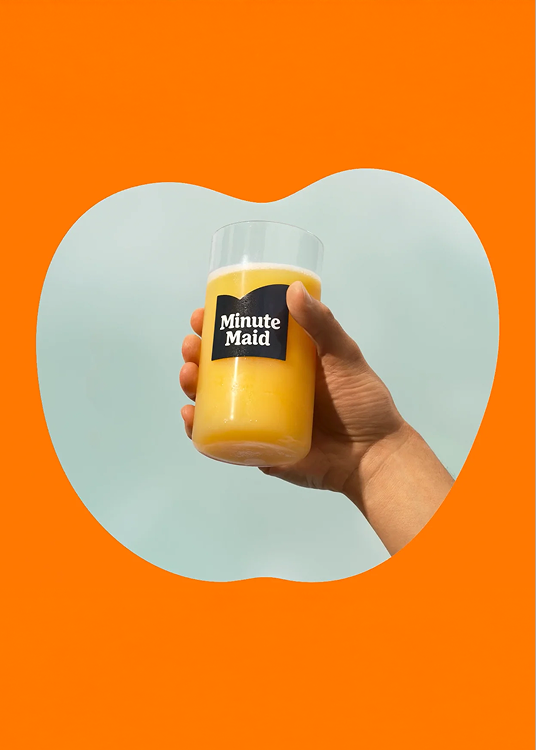 Een hand houdt een fles Minute Maid sinaasappelsap vast tegen een feloranje achtergrond.