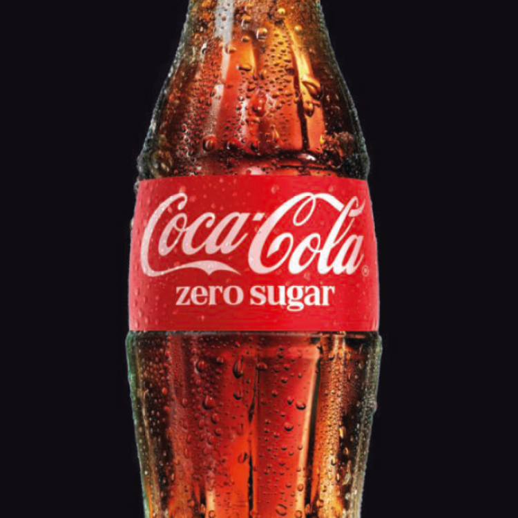 Une bouteille en verre Coca‑Cola Zero Sugar bien fraîche, avec des gouttelettes de condensation, sur un fond sombre.
