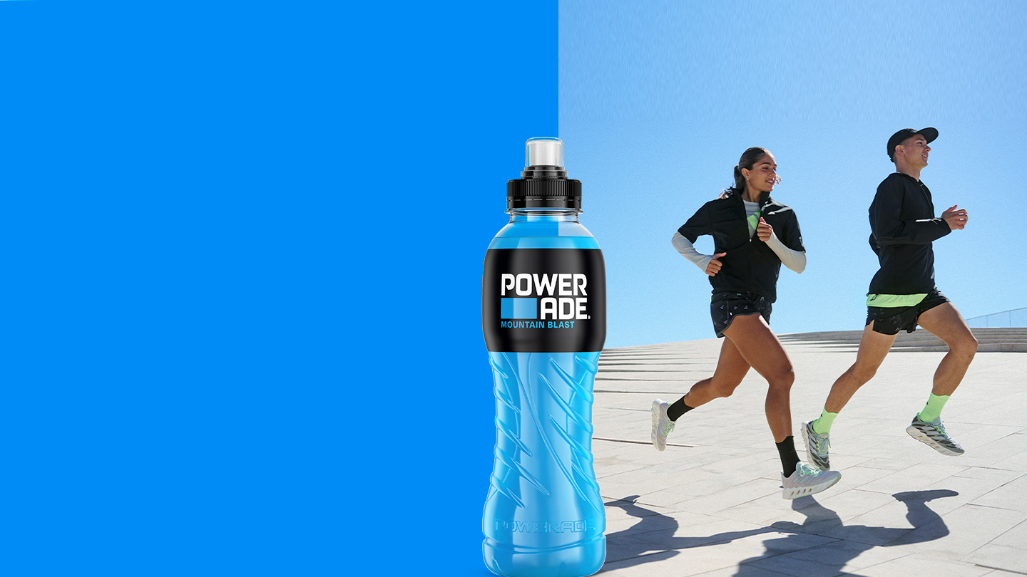 Een afbeelding met links een fles Powerade met de smaak "Mountain Blast" tegen een felblauwe achtergrond. Rechts rennen twee mensen in een sportieve omgeving op een zonnige dag. Ze dragen sportkleding en hardloopschoenen, terwijl ze in beweging zijn op een betegeld oppervlak.