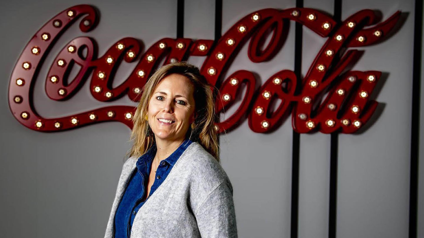 Een vrouw die voor het coca-cola-logo staat