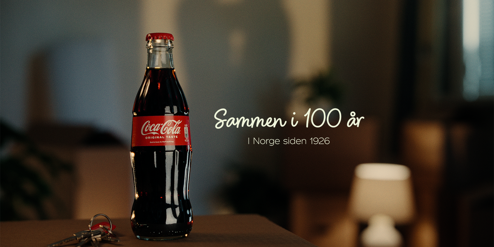 Coca-Cola flaska mot mörk bakgrund med texten Sammen i 100 år