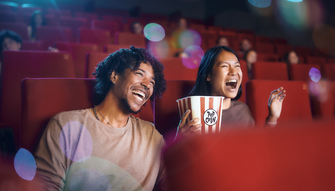 To personer ser på film på kino og ler og holder popcorn