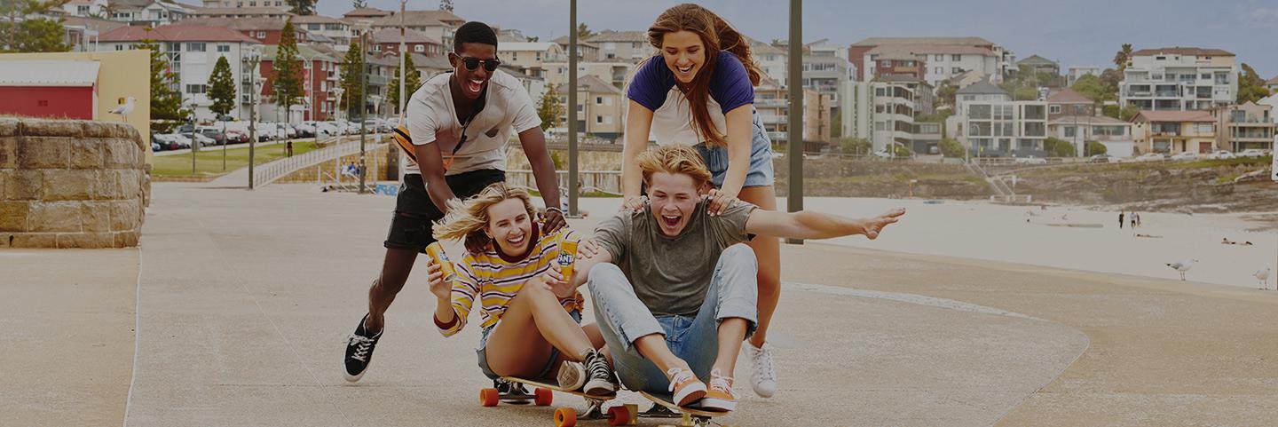 Group of four people laughing and playing with skateboards while holding Fanta cans