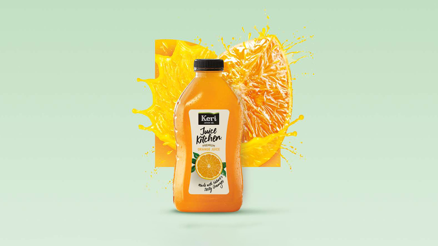 A Keri Premium Orange Juice bottle and on a wooden table with a fork, a knife, and a plate on the left