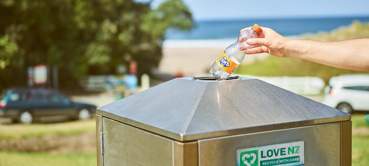A person putting an empty bottle of Fanta in a trash can 