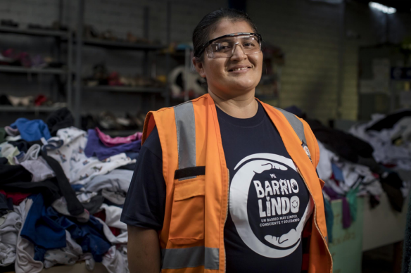 Mujer posa sonriente con montañas de ropa de fondo