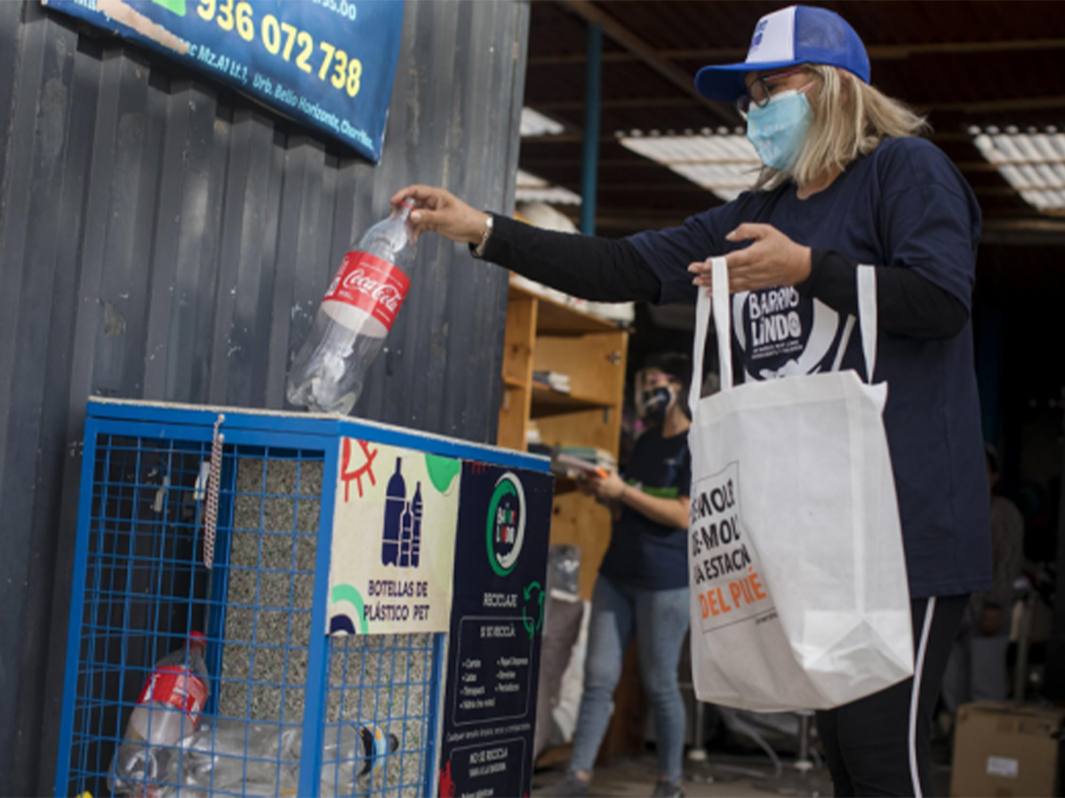 Mujer desechando botella de Coca-Cola en punto limpio