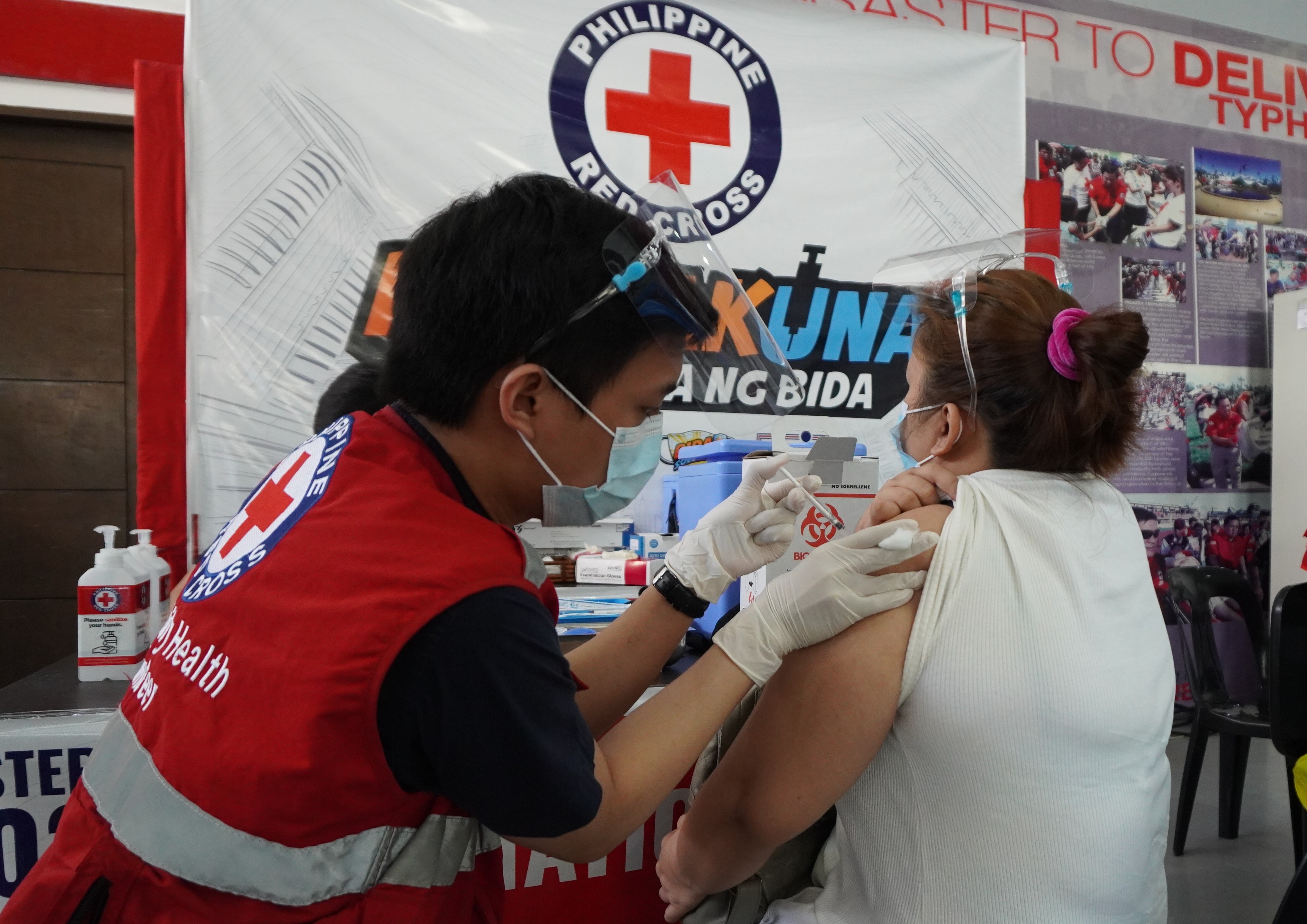 A man with a Philippine Red Cross vest giving a vaccine to a woman