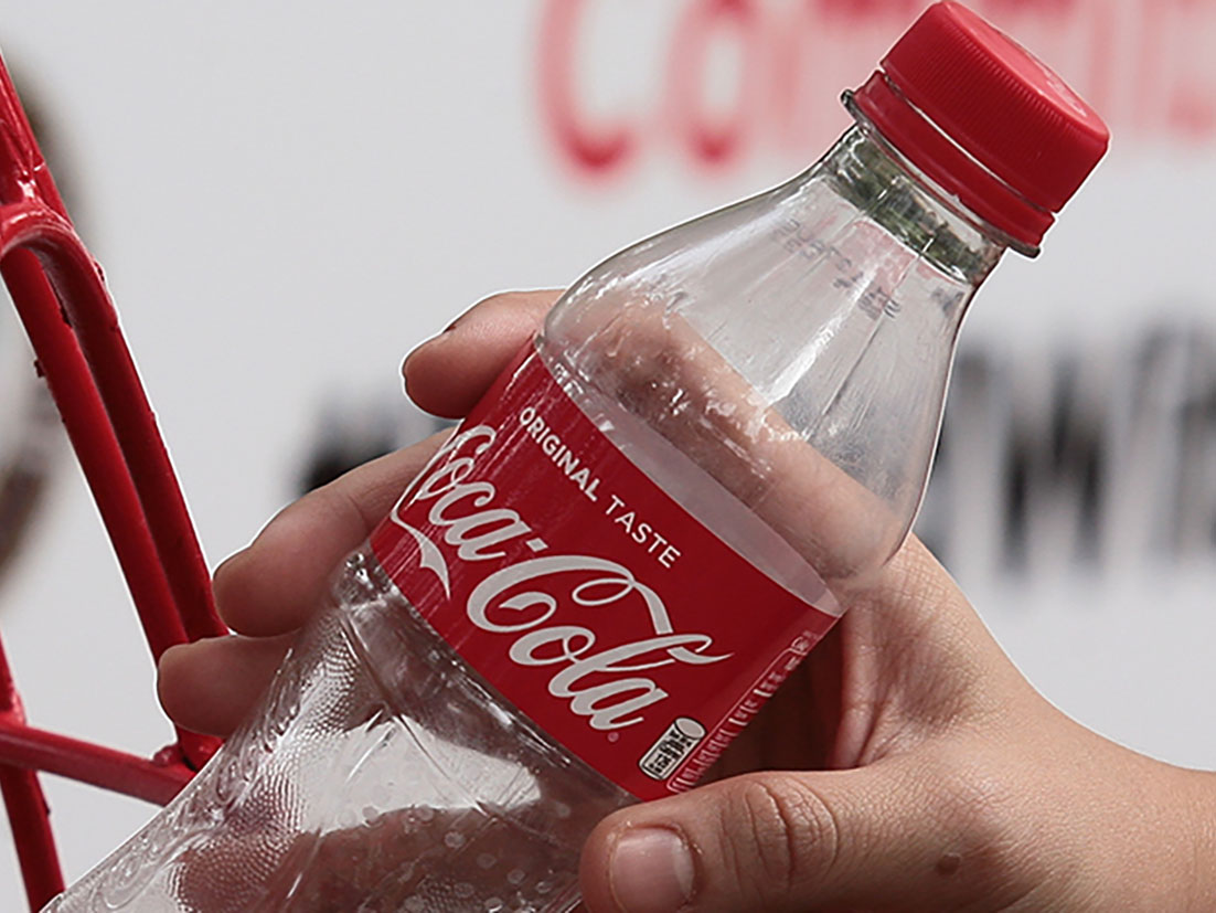 Detail of a hand putting an empty Coca-Cola plastic bottle in a recyclable trash bin