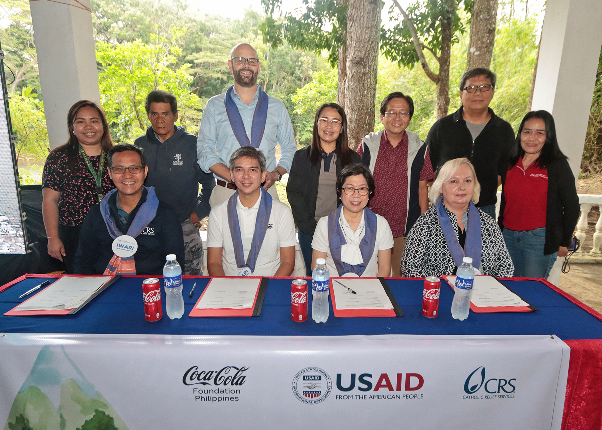 A group of people behind a table at a Coca-Cola Foundation Philippines, USAID, and CRS Philippines presentation
