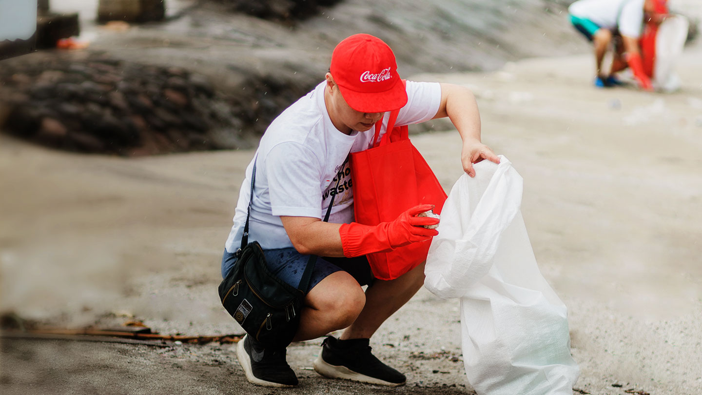  Crouched person wearing red hat while collecting waste in plastic bag