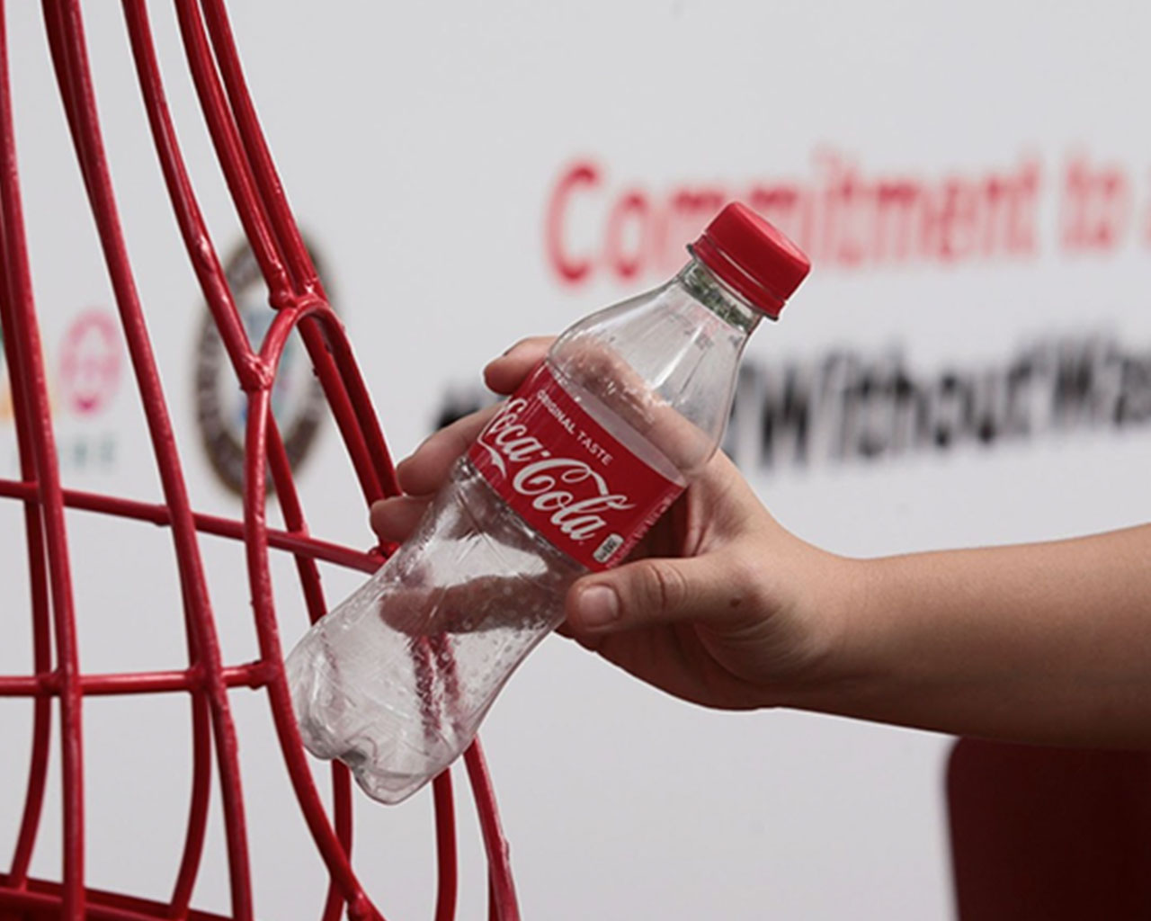 Someone putting an empty Coca-Cola bottle inside a red grid trash can