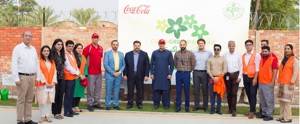A group of people standing in front of a Coca-Cola Clean Green Pakistan banner