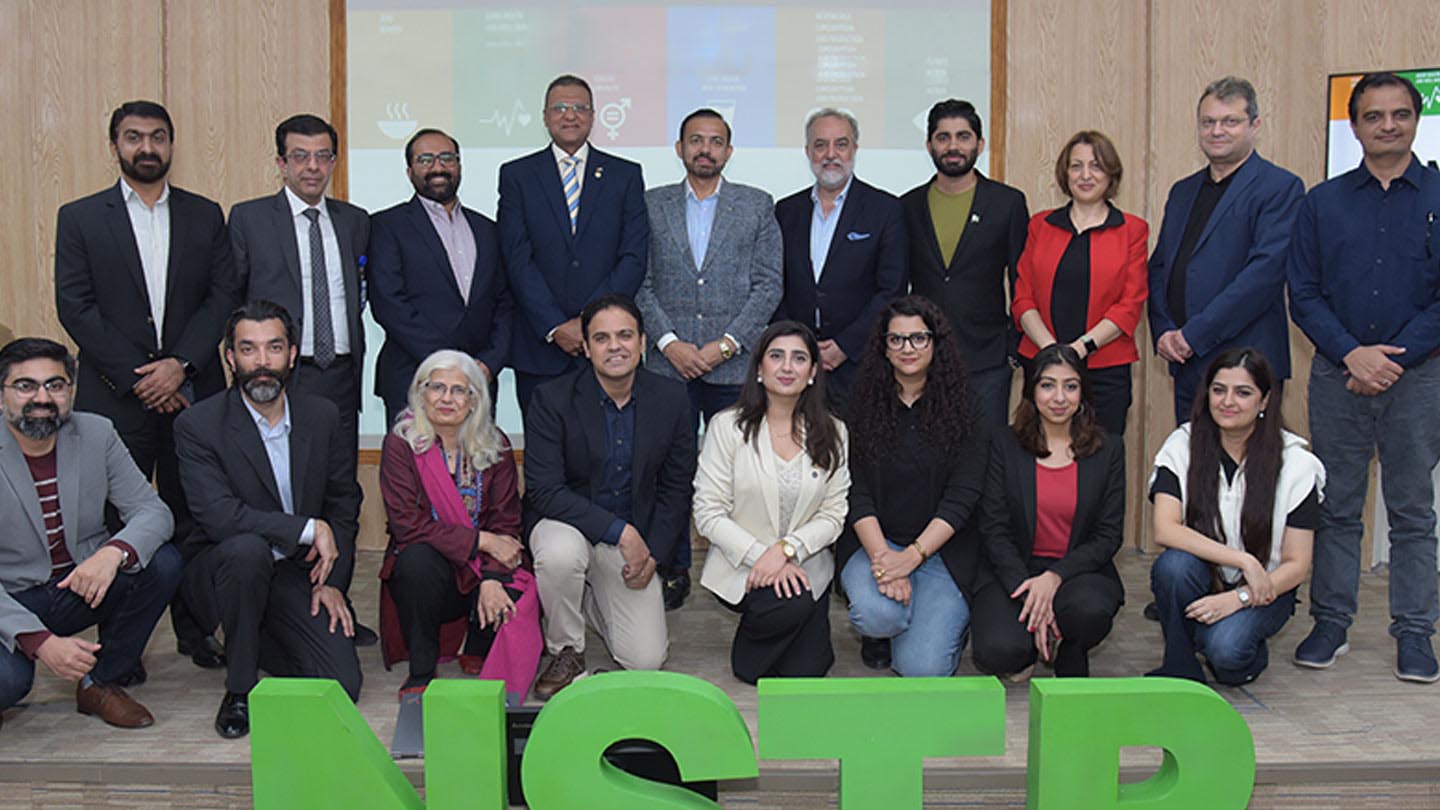 Group of people posing for a photograph on a small stage during the NUST seminar