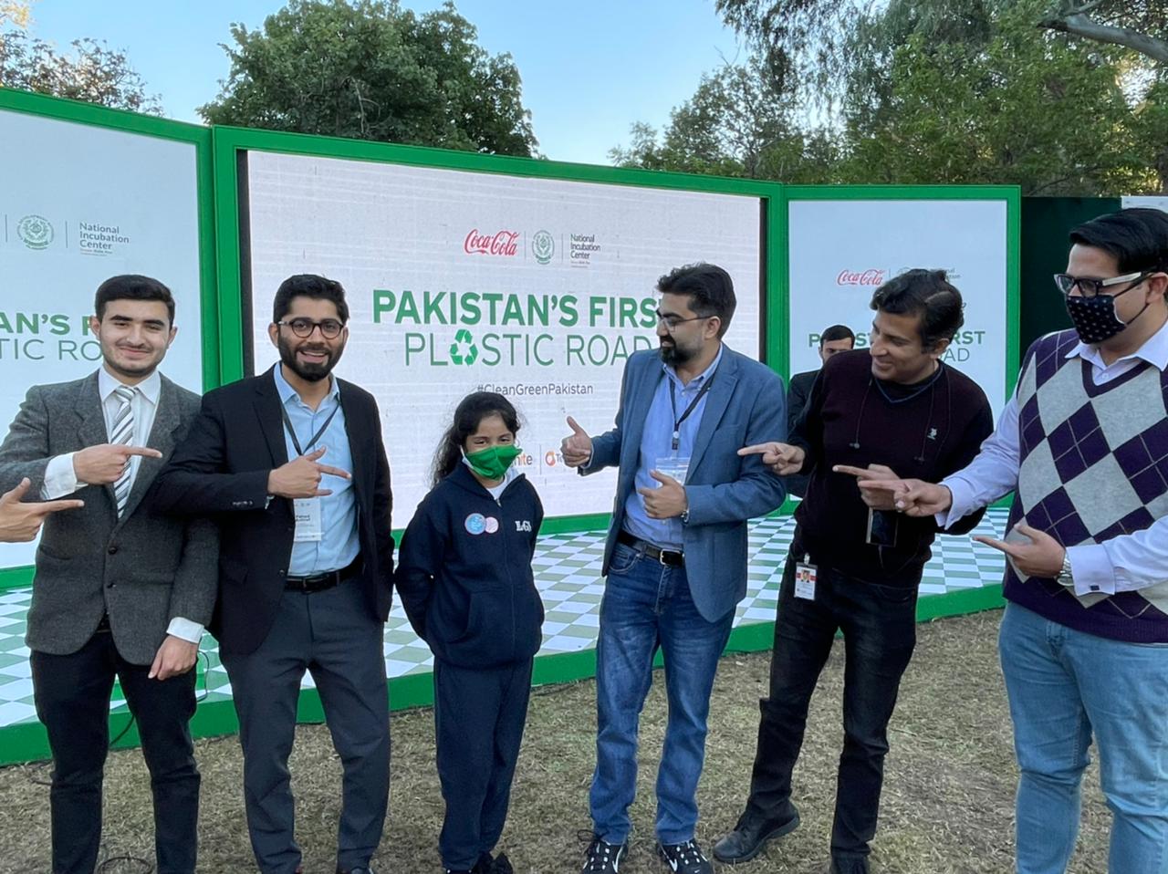 A group of people in front of a banner that says 'Pakistan's First Plastic Road'