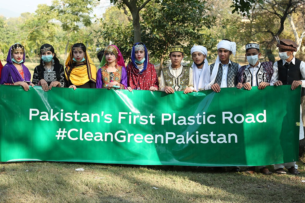 A group of people holding a banner with the following phrase 'Pakistan's First Plastic Road #CleanGreenPakistan'
