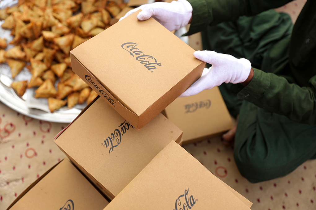 A person holding a carton box with the Coca-Cola logo