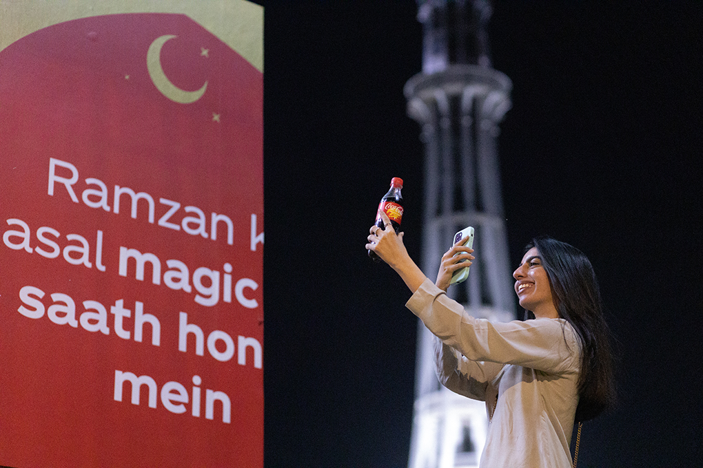 A woman making a cellphone photo of a Coca-Cola bottle