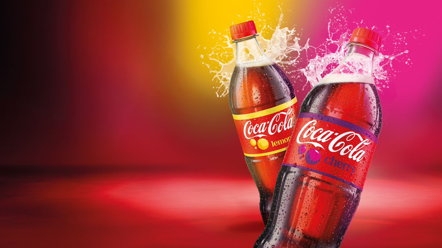 Divas Coca-Cola Lemon un Coca-Cola Cherry dzērienu pudeles ar dzērienu šļakatām uz krāsaina fona.