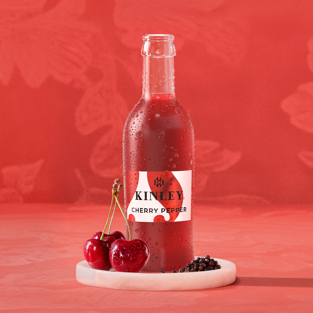 Butelka Kinley Cherry Pepper z kroplami wody na czerwonym tle z wiśniami.