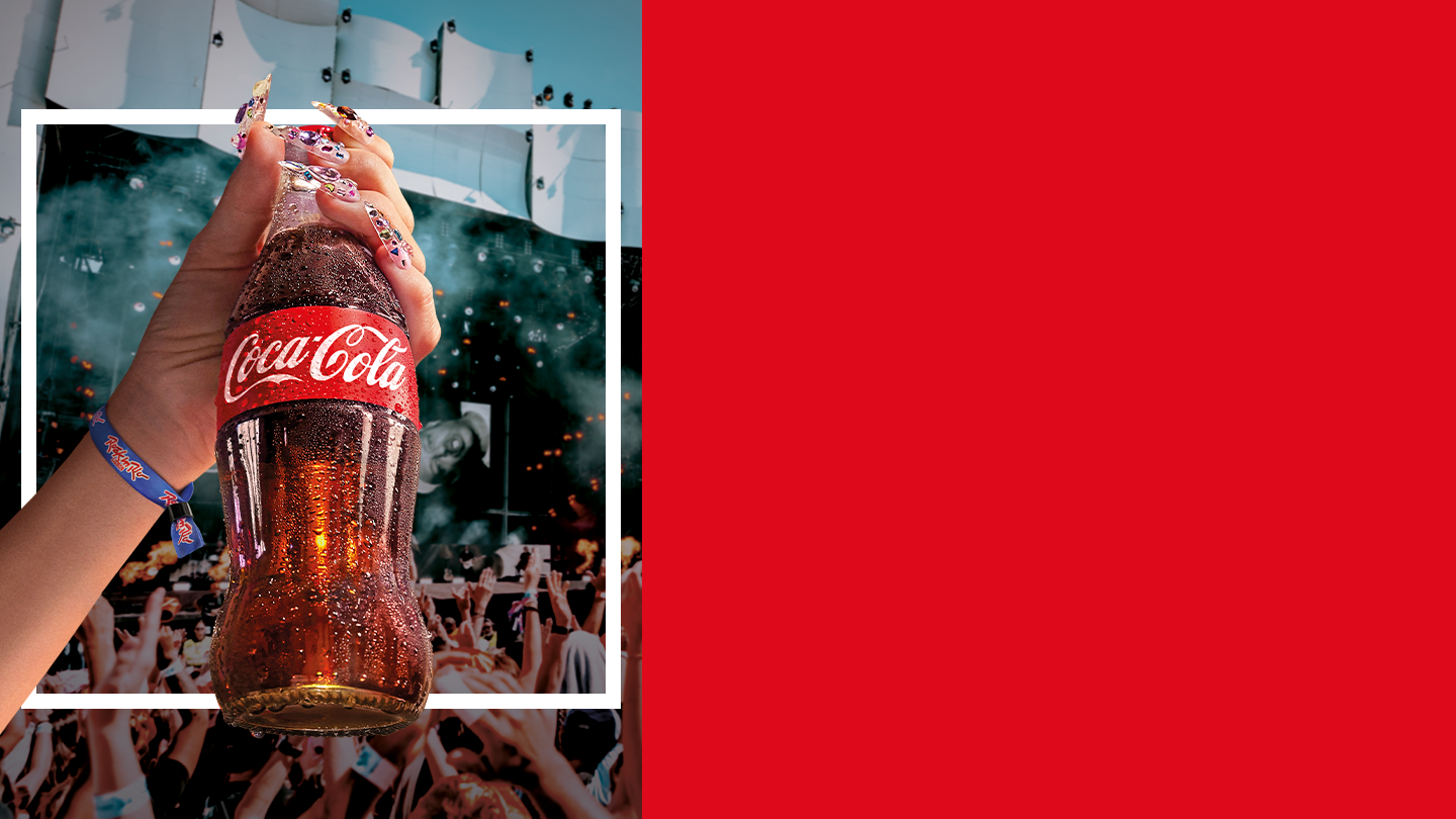 Pessoa a levantar uma garrafa de Coca‑Cola durante um concerto com o público em festa, representando a campanha Coca‑Cola Rock in Rio Lisboa 2026.
