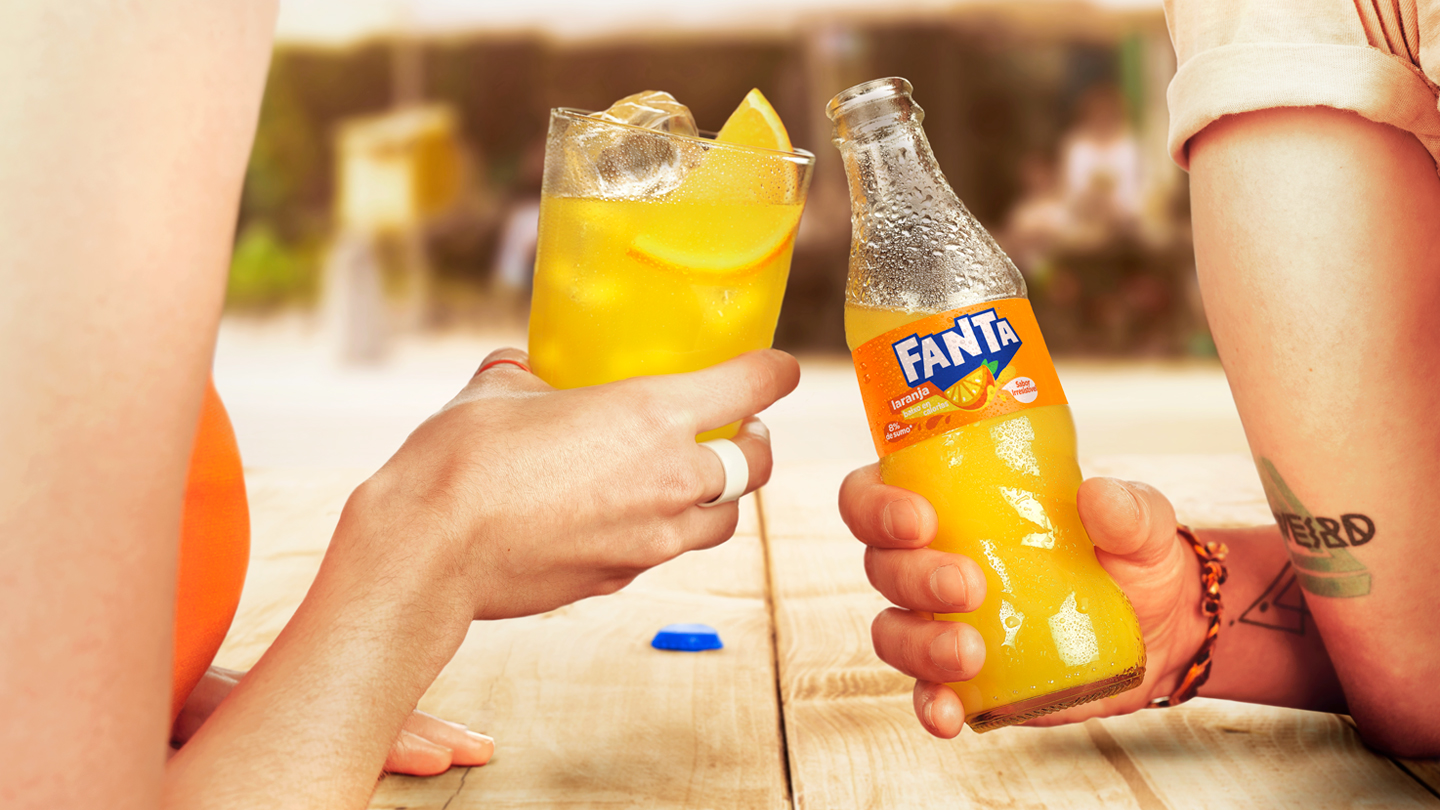 Duas pessoas brindando com um copo e uma garrafa de Fanta