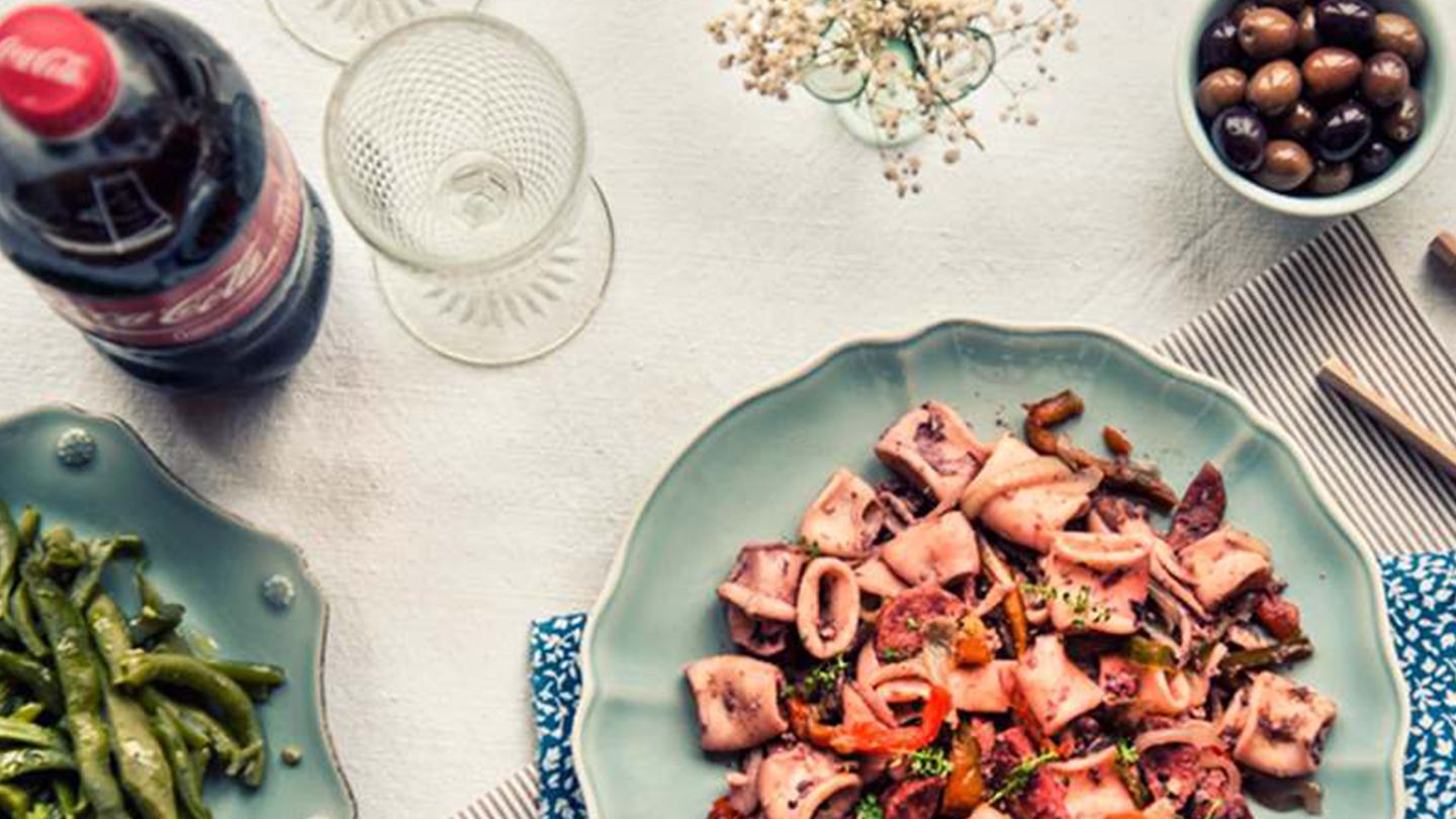 Pratos de comida em uma mesa com taças e uma garrafa de Coca-Cola