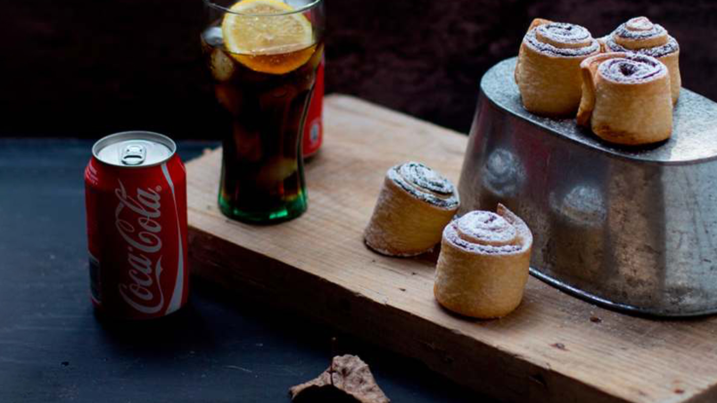 Uma bandeja de cinnamon rolls ao lado de um copo de refrigerante e uma lata de Coca-Cola