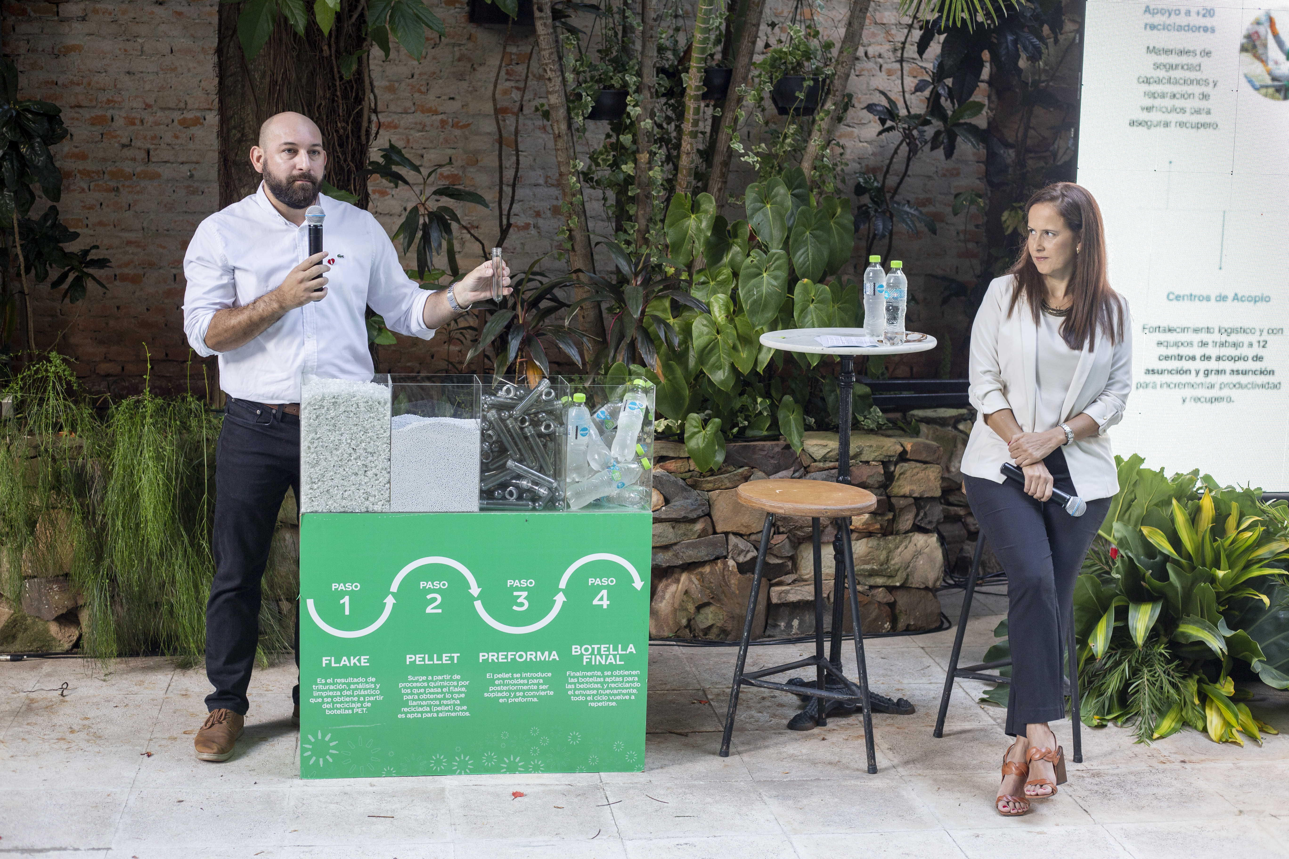 Hombre hablando en un evento y mujer sentada a su lado
