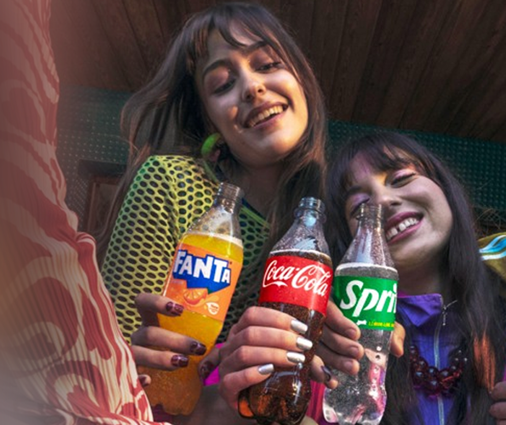 Mai multe persoane ciocnesc doze de Fanta, Coca‑Cola și Sprite.