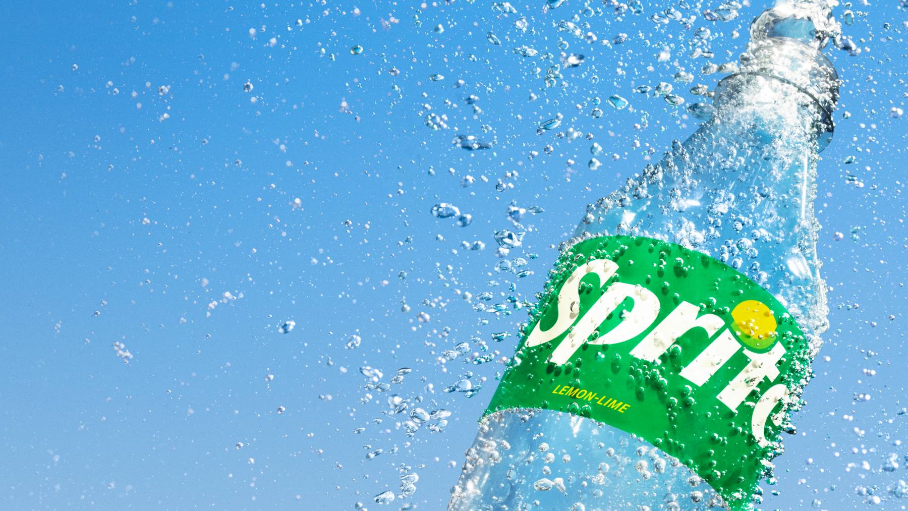 Sticla/doza de Sprite pe un background imitand cerul, cu stropi in jurul ei