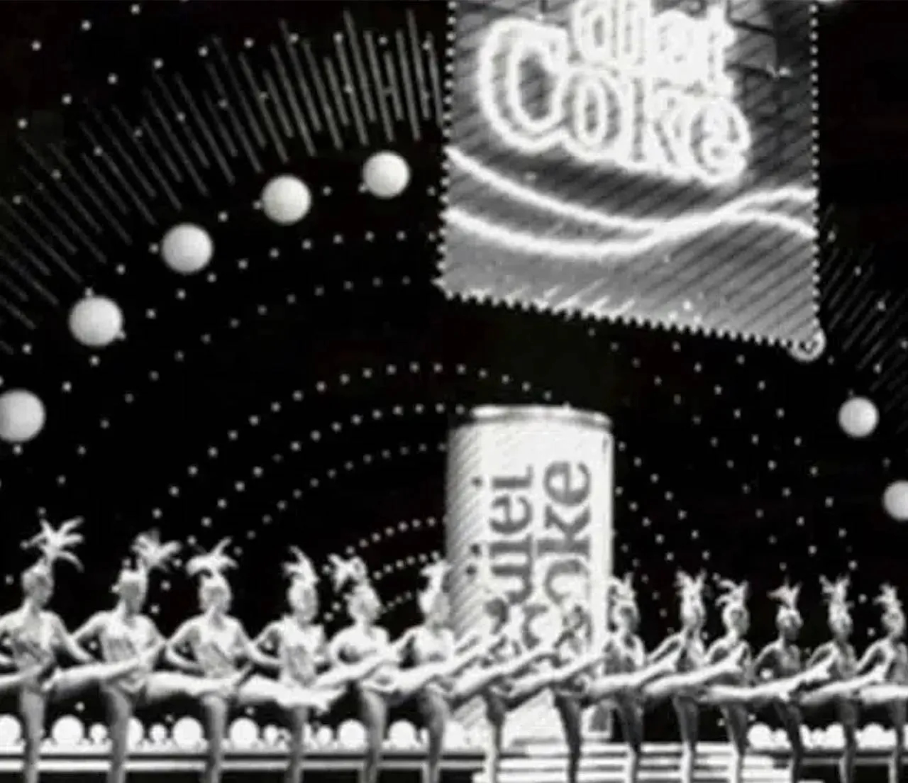 Scenă în alb-negru de la un spectacol de revistă, în fundal apare o imensă doză de Coca-Cola Light