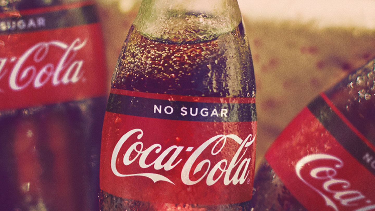 Detail of a Coca-Cola No Sugar glass bottle with two other bottles blurred in the background