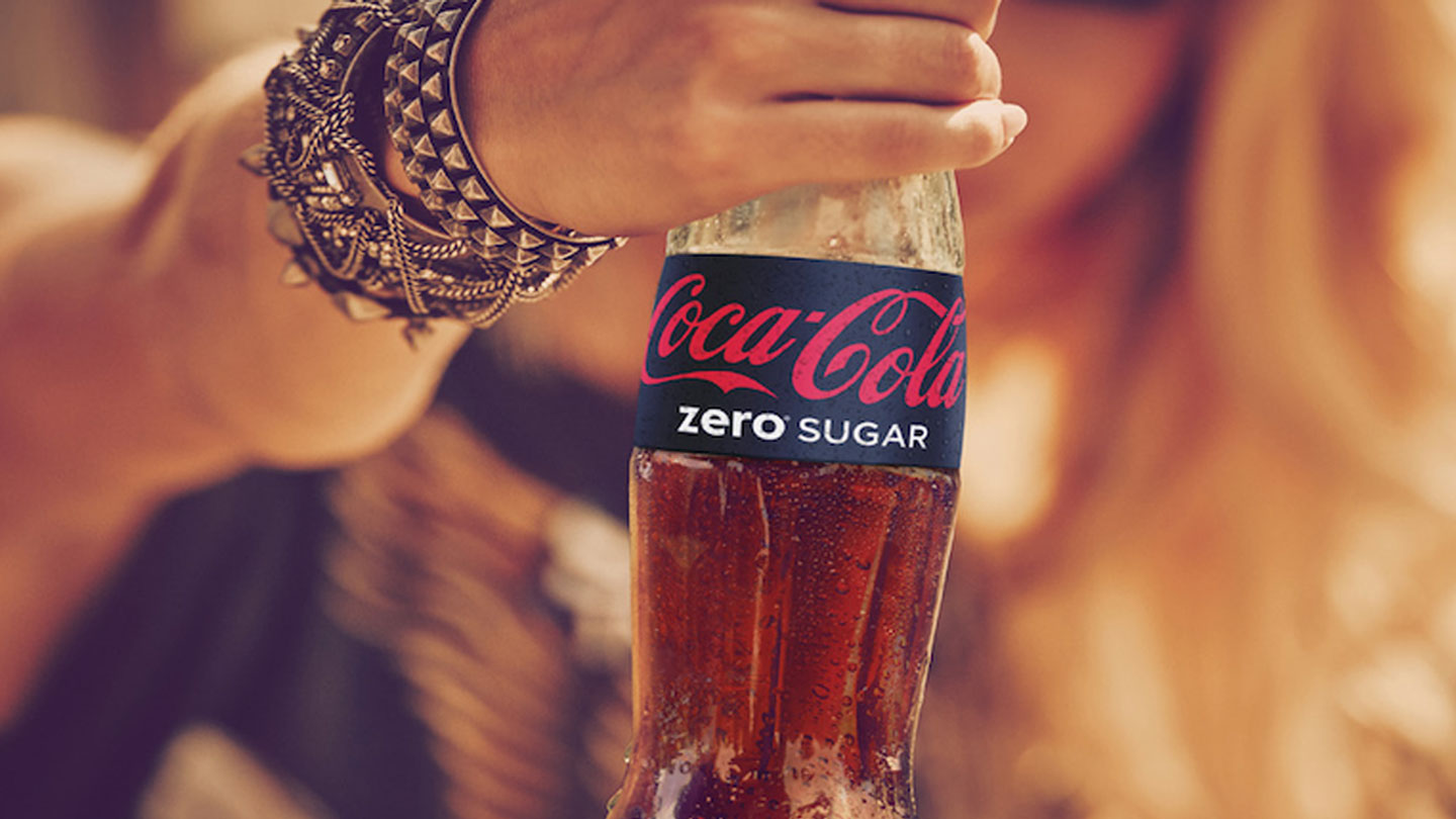 A close-up at the hand of a woman holding a Coca-Cola Zero Sugar bottle