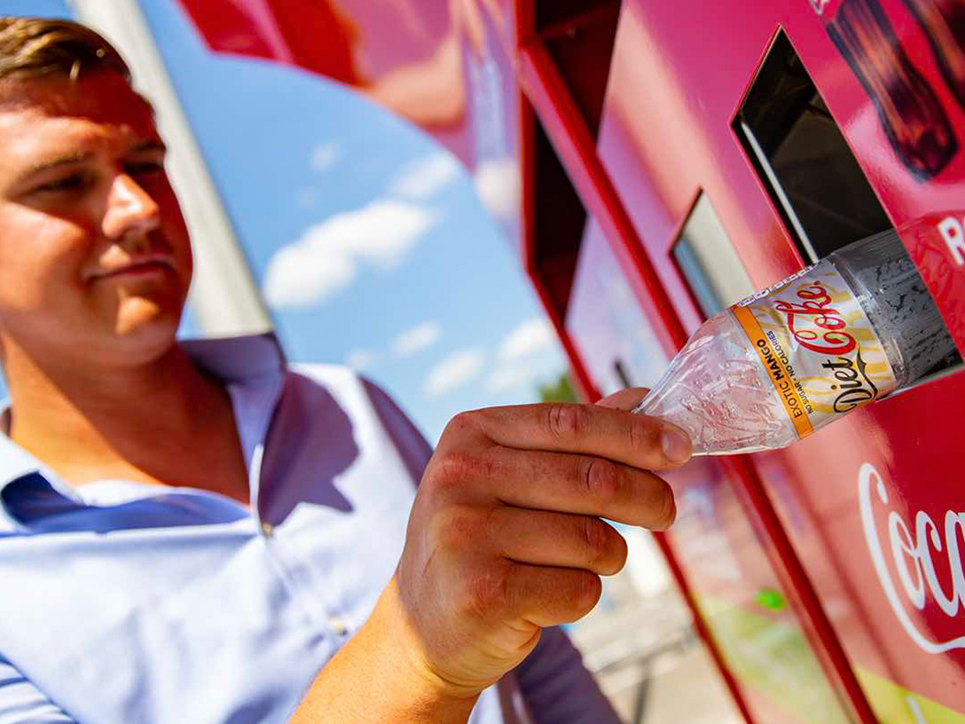 Detail of a hand putting an empty Coca-Cola plastic bottle in a recyclable trash bin