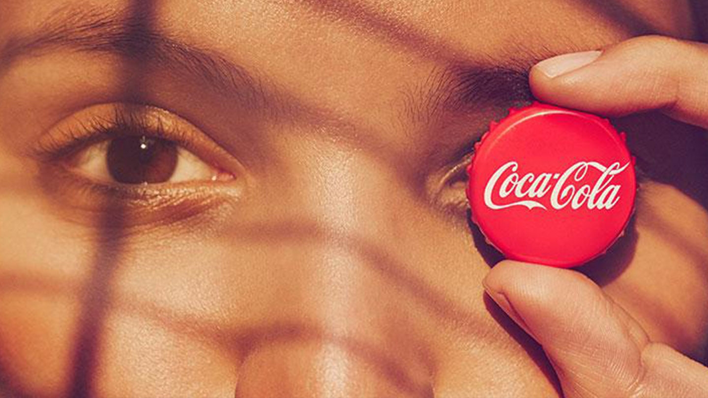 Žena, ktorá má na oku uzáver fľaše od nápoja Coca-Cola