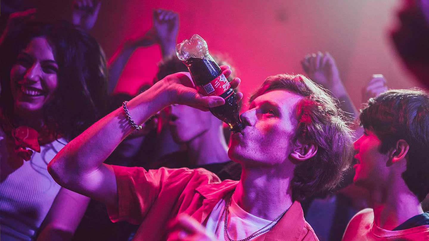 Mladý muž pije z fľaše Coca-Cola Zero Sugar na párty.