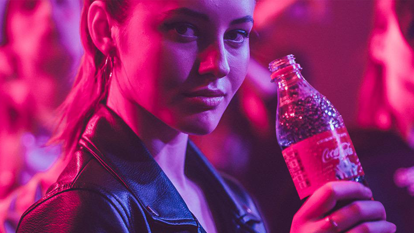 Obrázok mladej ženy, ktorá si užíva fľašu nápoja Coca-Cola na párty.