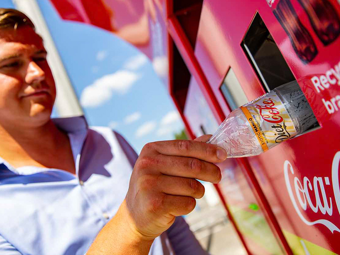 Muž vkladá použitú plastovú fľašu Coca-Coly do zberného koša na recykláciu
