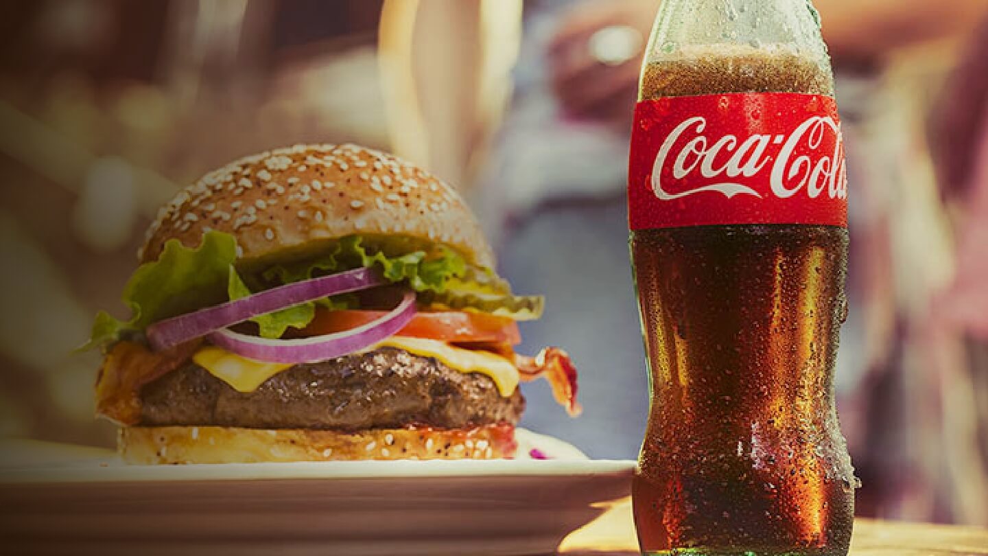 A hamburger and a Coca-Cola Classic bottle on a table