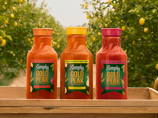 Three Simply Gold Peak Real Brewed Tea bottles displayed on a wooden tray in a lemon orchard.
