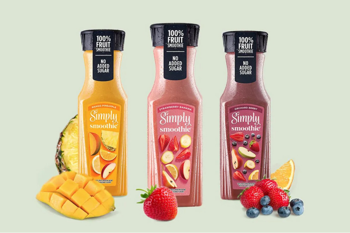 Three containers of different Simply smoothie flavors with fruit in the background and foreground