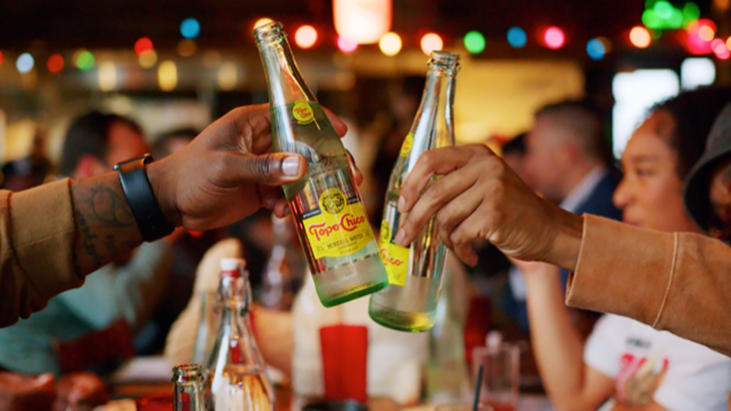 Detail of two hands toasting with Topo Chico bottles in Hojoko tavern