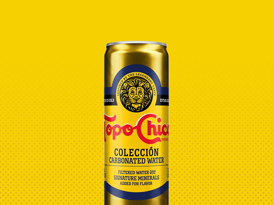 A condensation-covered gold can of Topo Chico Colección Carbonated Water is centered against a solid yellow background with a subtle dot pattern in the lower right.